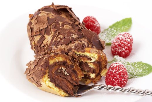 Miniature chocolate swiss roll cake served on a plate with mint leaves and raspberries on white background
