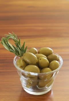 Jar of green olives and rosemary on wooden table background