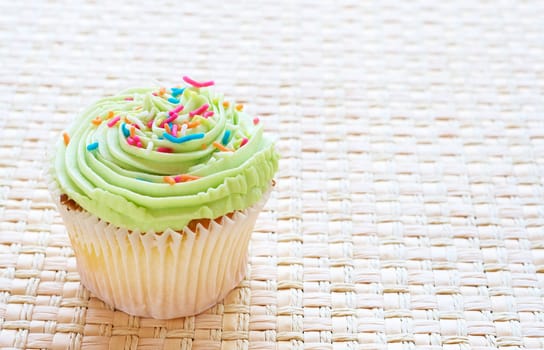 Fresh vanilla cupcake with lime icing on woven straw background