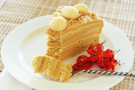 Slice of Caramel Medovik cake made of honey and caramel cream, decorated with flowers