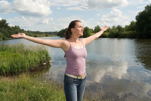 The young woman has stretched hands on a background of the river.