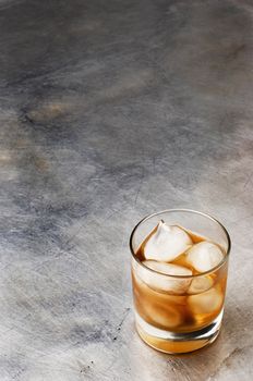one shot of whiskey on the rocks, over metallic scratched surface