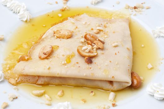 folded pancake floating in honey in dish, with almonds and creme
