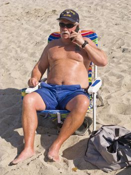 Senior Man using a Cell Phone on the Beach while sitting in his Chair