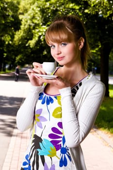 Smiling lovely young woman drinking coffee outside