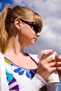 Blond lovely young woman drinking cup coffee outside