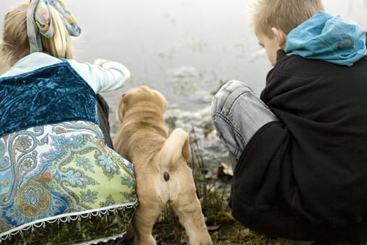 Brother and sister playing at the lake while sharpei puppy is watching