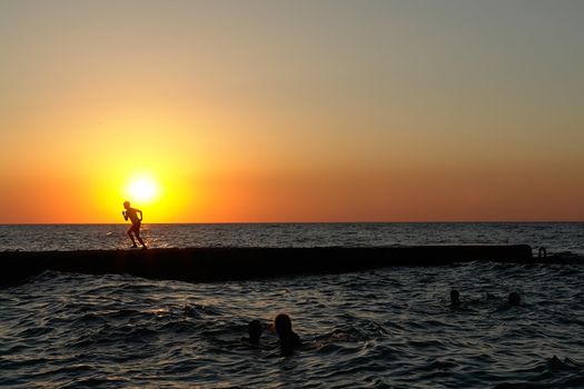 the boy runs on a pier on a background of a sunset