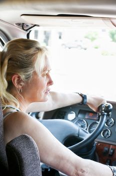 Blonde woman in her forties looking to the right making a turn in a big truck.