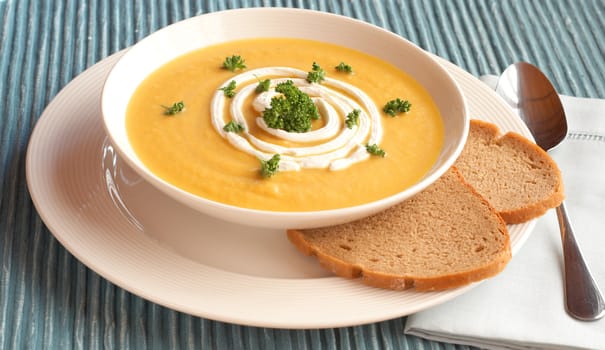 Bowl of fresh hot butternut soup with cream and parsley, served with rye berliner bread