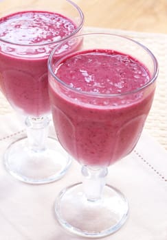 Two glasses of fresh berry smoothies on hessian placemat background