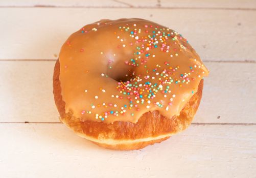 Donut covered in caramel icing and sprinkles on grunge wooden background