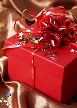 Red gift box with bows and stars on golden silk background