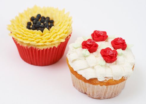 Two vanilla cupcakes with various decorations on white background