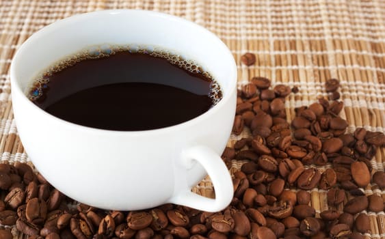 Cup of fresh brewed coffee with roasted coffee beans on straw placemat