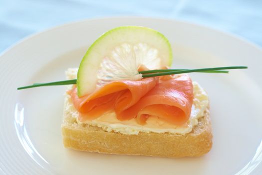 Smoked salmon and cream cheese on white bread with slice of lemon and chives