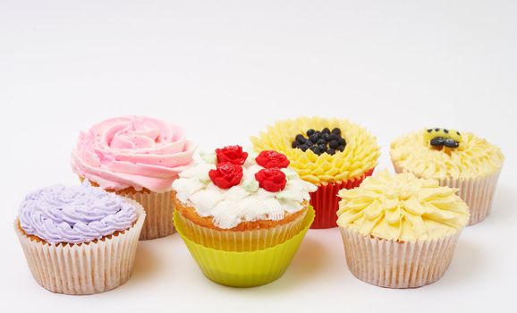 Variety of vanilla cupcakes with various decorations on white background