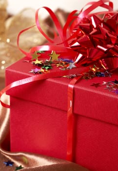 Red gift box with bows and stars on golden silk background