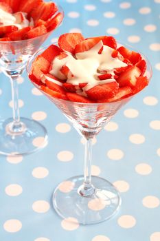 Sliced fresh strawberries with running cream in martini glasses on blue polka dot background