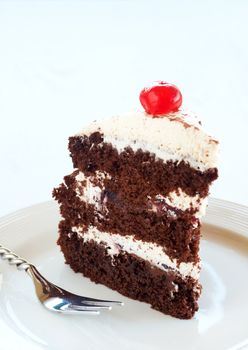 Slice of Black Forest cake with fresh cream and cherries, served on a white plate with silver fork