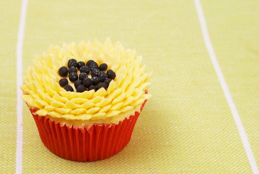 Fresh vanilla cupcake with sunflower buttercream icing decoration on green background