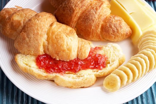 Breakfast plate with freshly baked croissants filled with jam, served with bananas and cheddar cheese slices