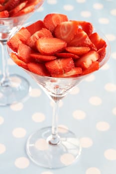 Sliced fresh strawberries in martini glasses on blue polka dot background