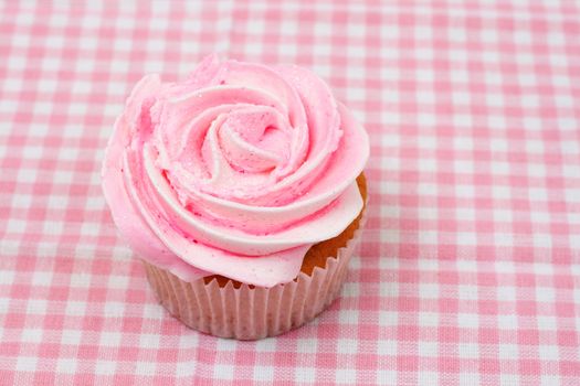 Fresh vanilla cupcake with pink rose icing on checkered background