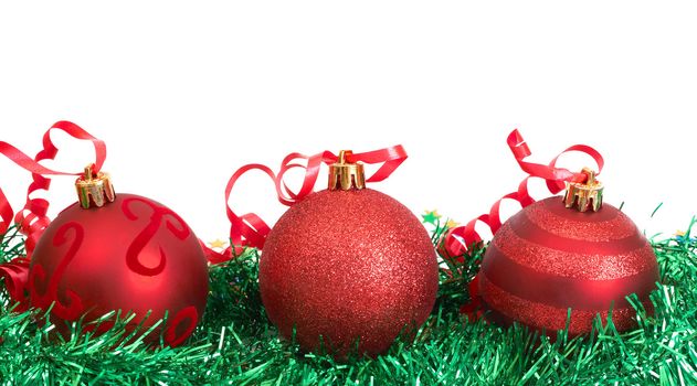 Three red Christmas baubles on green tinsel isolated on white background with copy space. 