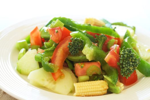 Fresh salad with cucumber, tomato, peppers, baby sweet corn and broccoli on white plate