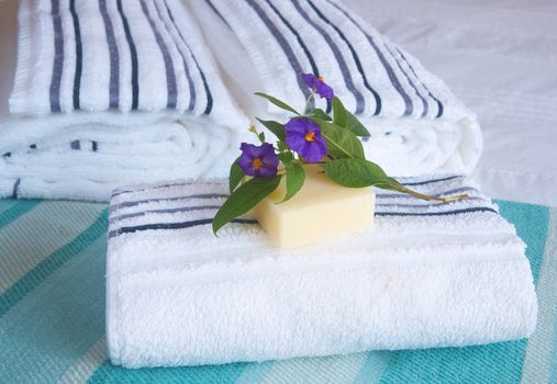 Beautiful bedroom interior with white sheets and striped towels with soap and flowers