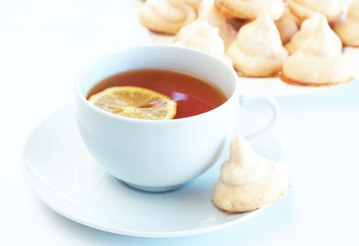 Cup of tea with lemon and meringue cookie on white background. Focus on the cup