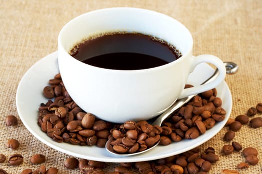 Cup of fresh brewed coffee with roasted coffee beans on straw placemat