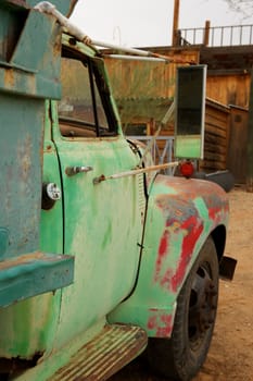 A rusty old truck with patches of green and red paint in a dirt lot