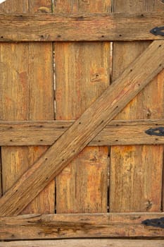 An old, weathered, worn, wooden gate with heavy grains, nail marks and black iron hinges