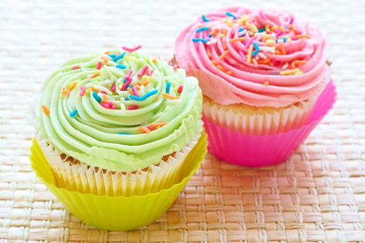 Fresh vanilla cupcakes with strawberry and lime icing on woven placemat background