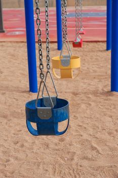 Colorful Empty Swings standing still with chainlink on a playground with sand