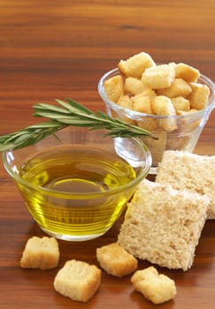 Two jars of olive oil with stick of rosemary and croutons on wooden table background