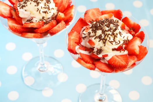 Sliced fresh strawberries and cream in martini glasses on blue polka dot background