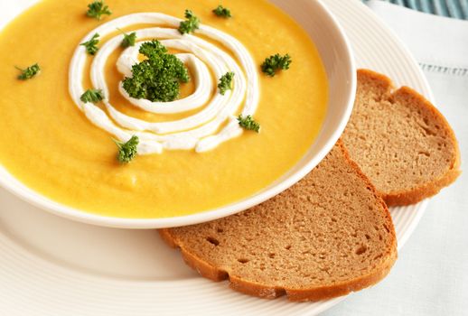 Bowl of fresh hot butternut soup with cream and parsley, served with rye berliner bread