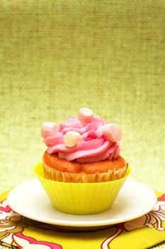 Fresh vanilla cupcake in green cup with strawberry icing and marshmallows on decorative background