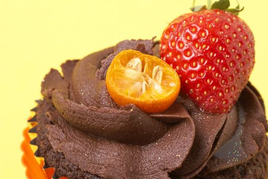 Chocolate cupcake with icing, fresh strawberry and orange rind on yellow background