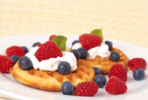 Belgian waffles with fresh raspberries, blueberries, mint leaves and cream on white plate