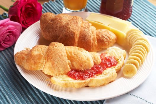 Breakfast plate with freshly baked croissants filled with jam and served with sliced bananas and cheddar cheese