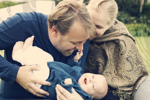 Beautiful happy family of three sitting on the grass laughing. Focus is on the father