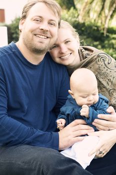 Beautiful happy family of three sitting on the grass smiling. Focus is on the father