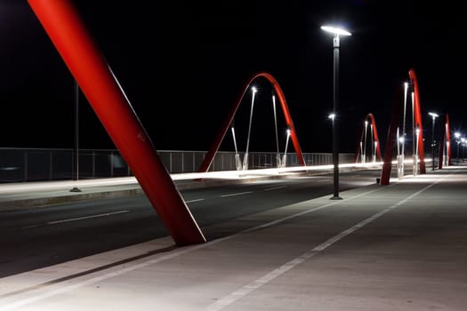 Steel arcs of modern urban road bridge illuminated at night.