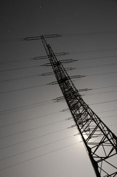 Steel pylon of high voltage electric power transmission line at moon lit night.