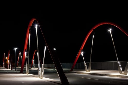 Steel arcs of modern urban road bridge illuminated at night.