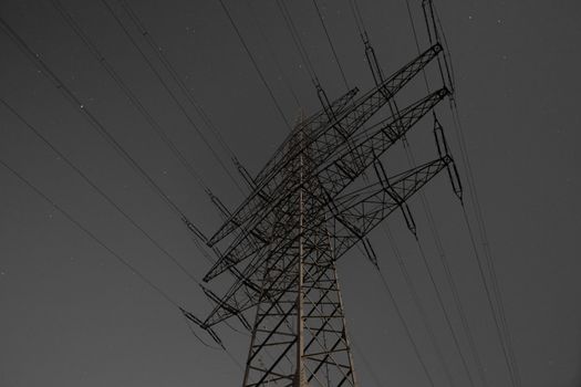 Steel pylon of high voltage electric power transmission line at moon lit night.